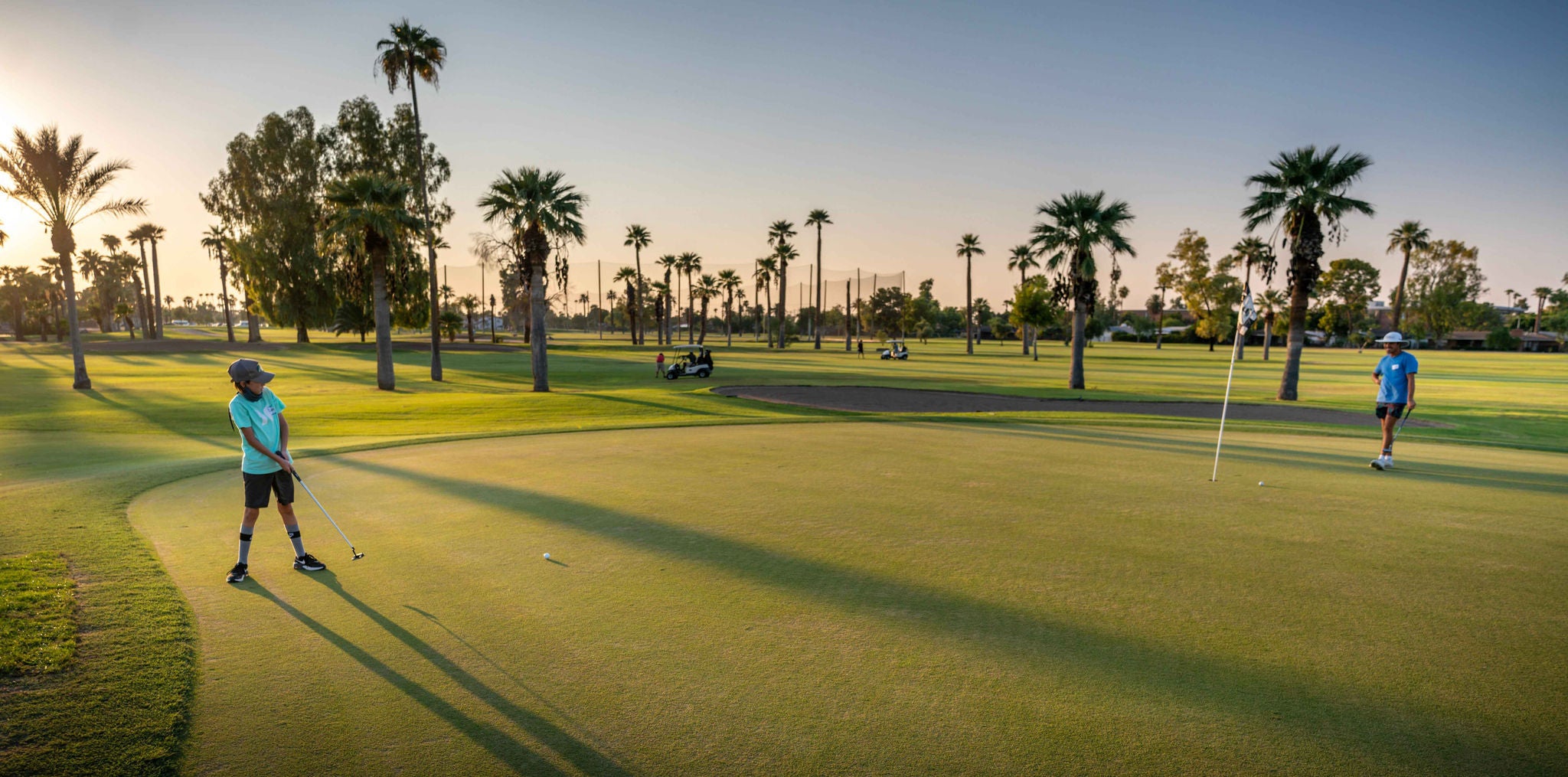 Two individuals play golf at sunset.